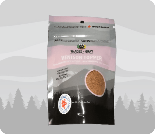 Image of Shades of Gray Indigenous Pet Treats' Venison Topper packaging, a pink bag with a mountain backdrop. Features 100% venison, raised without antibiotics, 100% natural, and free of glycerine, gluten, grain, and preservatives. Includes 'Made in Canada' and 'Ontario' badges, with a paw print logo and net weight of 3 oz."