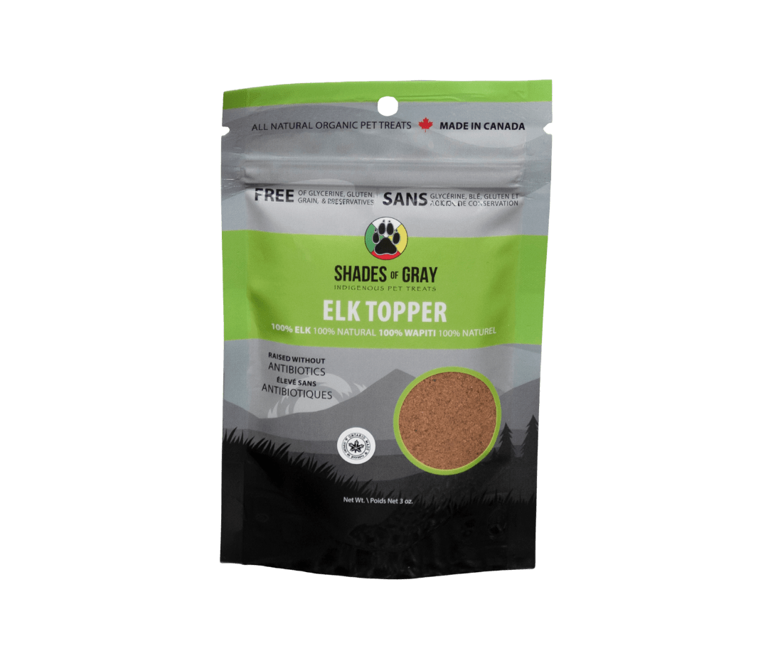Front of Shades of Gray Indigenous Pet Treats Elk Topper packaging in premium matte black and grey with lime green resealable pouch, featuring bold white “ELK TOPPER” lettering, single-ingredient callout, clear window revealing air-dried elk meat in granular form, Made in Ontario badge, Canadian flag, and circular Shades of Gray Indigenous Pet Treats logo.