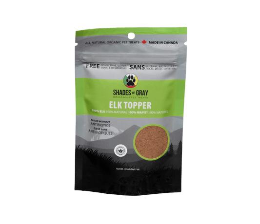 Front of Shades of Gray Indigenous Pet Treats Elk Topper packaging in premium matte black and grey with lime green resealable pouch, featuring bold white “ELK TOPPER” lettering, single-ingredient callout, clear window revealing air-dried elk meat in granular form, Made in Ontario badge, Canadian flag, and circular Shades of Gray Indigenous Pet Treats logo.