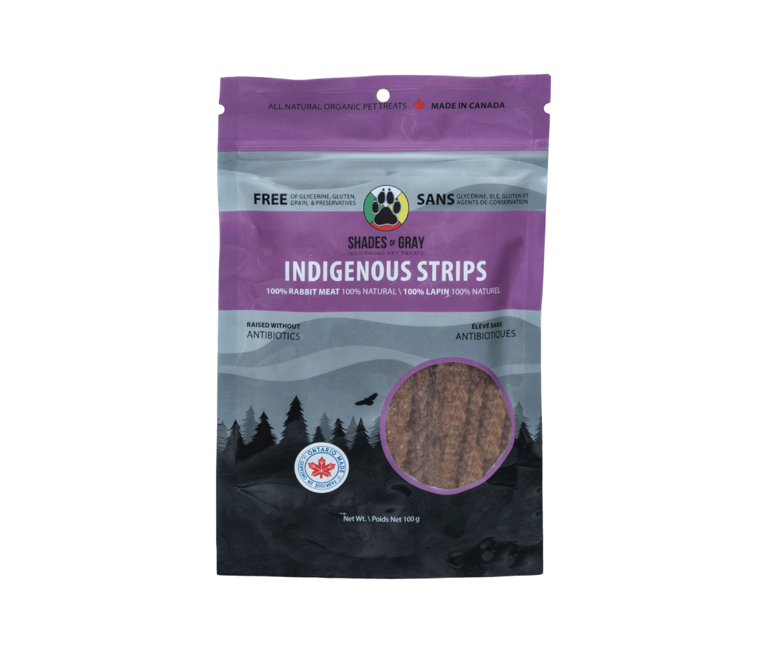 Image of Shades of Gray Indigenous Pet Treats' Indigenous Strips rabbit pet treats packaging, featuring 100g bag of rabbit strip pet treats. The text on bag highlights 100% rabbit meat, raised without antibiotics, 100% natural, and free of glycerine, gluten, grain, and preservatives. 'Made in Canada' and 'Ontario' badges are visible, with a paw print logo and net weight of 100g