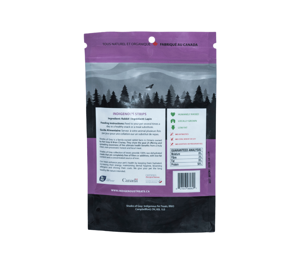 Back view of Shades of Gray Indigenous Pet Treats' Indigenous Strips packaging, a purple bag of rabbit pet treats with 'Made in Canada' label. Highlights 100% rabbit meat, humanely raised, locally grown, low fat, no antibiotics, corn, wheat, soy, or additives. Includes feeding instructions, guaranteed analysis (3% moisture, 9% fiber, 50% protein), and certifications from My Pick Local Farmer and Aboriginal Business.