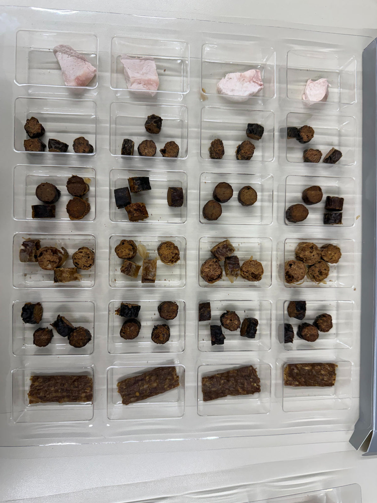 Inside the Shades of Gray Cat Christmas Advent Calendar: a clear tray of compartments holding small, single-ingredient meat treats. Rows of Freeze-Dried Rabbit, bite-sized Rabbit, Elk, Bison, and Venison Cat Treats, and Rabbit Strips, with one compartment for each day from December 1 to 24.