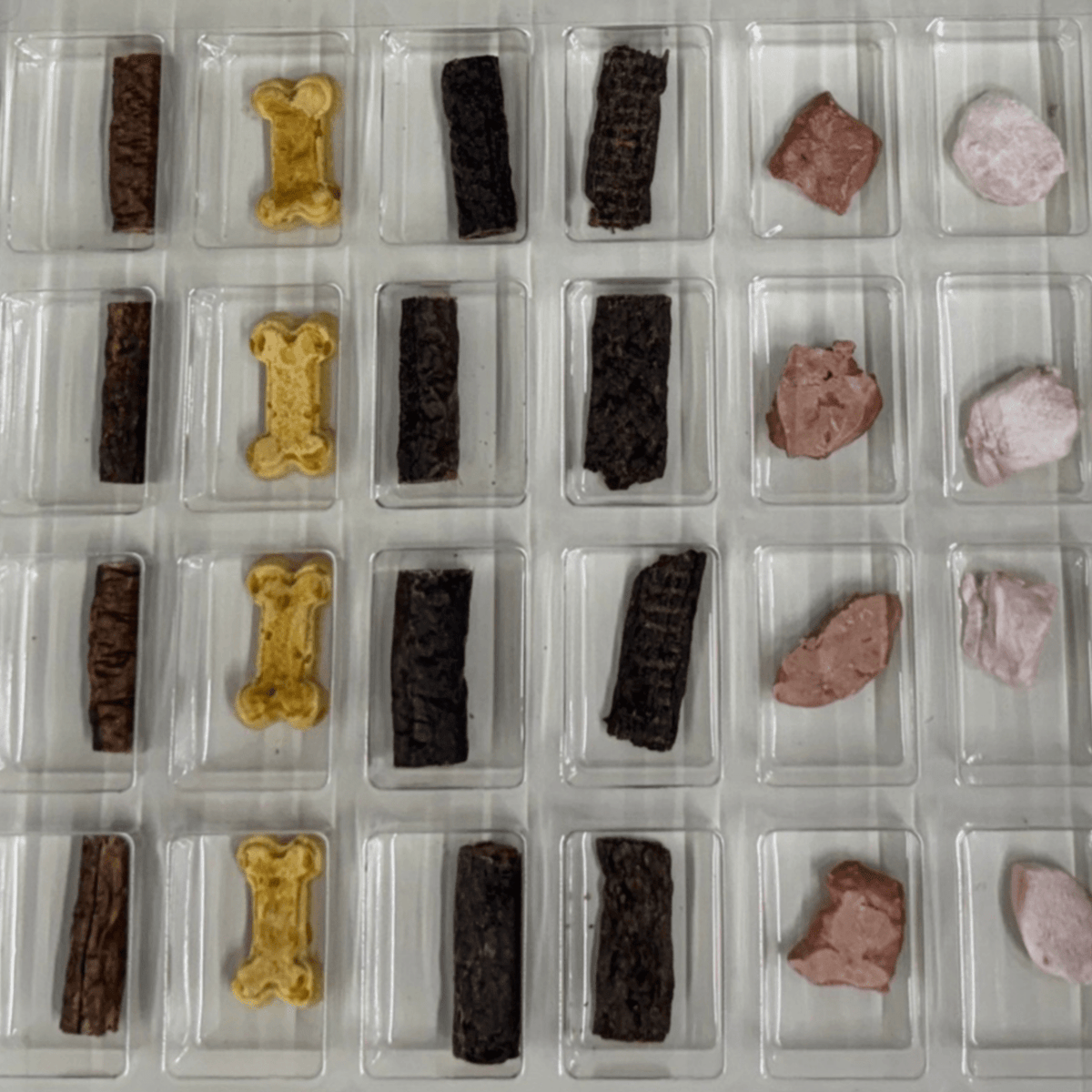 Inside the Shades of Gray Dog Christmas Advent Calendar: a clear tray of compartments, each holding one treat. Rows of Venison Strips, Waboose rabbit biscuits, Beaver Rolls, Elk Rolls, Freeze-Dried Bison Liver, and Freeze-Dried Rabbit, one behind each door from December 1 to 24.