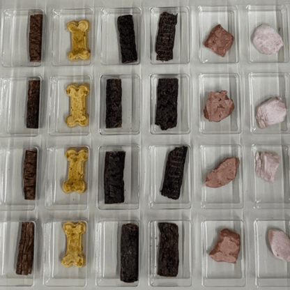 Inside the Shades of Gray Dog Christmas Advent Calendar: a clear tray of compartments, each holding one treat. Rows of Venison Strips, Waboose rabbit biscuits, Beaver Rolls, Elk Rolls, Freeze-Dried Bison Liver, and Freeze-Dried Rabbit, one behind each door from December 1 to 24.