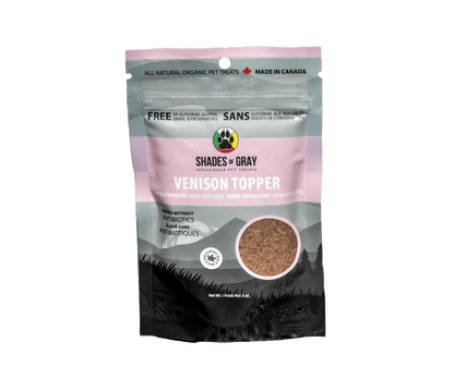 mage of Shades of Gray Indigenous Pet Treats' Venison Topper packaging, a pink bag with a mountain backdrop. Features 100% venison, raised without antibiotics, 100% natural, and free of glycerine, gluten, grain, and preservatives. Includes 'Made in Canada' and 'Ontario' badges, with a Shades of Gray Indigenous Pet Treats paw print circular logo and net weight of 3 oz."