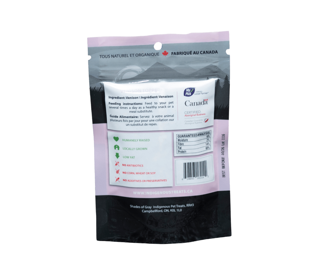 Back view of Shades of Gray Indigenous Pet Treats' Venison Topper packaging, a pink bag with 'Made in Canada' label. Highlights 100% venison, humanely raised, locally grown, low fat, no antibiotics, corn, wheat, soy, or additives. Includes feeding instructions and guaranteed analysis (16% moisture, 2% fiber, 14% fat, 60% protein).